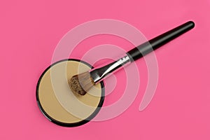 make-up powder and brush on pink background, top view
