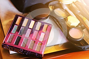 Make-up products and cosmetics with Palette with colorful eyeshadows, Brushes, lipgloss, lipstick on wood table