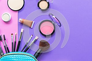 Make up products spilling out of a pastel blue cosmetics bag, on purple and pink background with empty space at side.