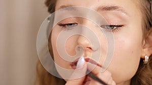 Make-up of a young girl`s face. Applying paint to the lips of the girl.