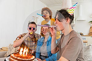 Make a wish. Woman wearing party cap blowing out burning candles on birthday cake. Happy Birthday party. Group of
