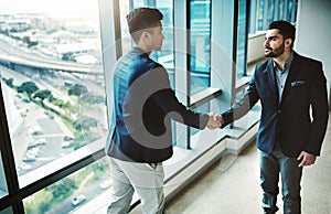Make your business grow with who you know. two young businessmen shaking hands in a modern office.