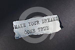 MAKE YOUR DREAMS COME TRUE - text on torn paper on dark desk in sunlight