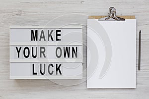 `Make your own luck` on a modern board, clipboard with blank sheet of paper on a white wooden background, top view. Flat lay, fr
