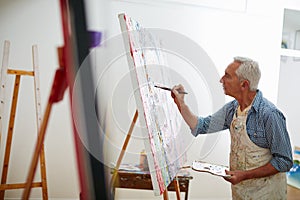 Makers gonna make. Shot of a senior man working on a painting at home.