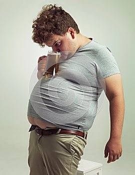 This makes drinking so much easier. an overweight man sipping a beer while it balances on his stomach.