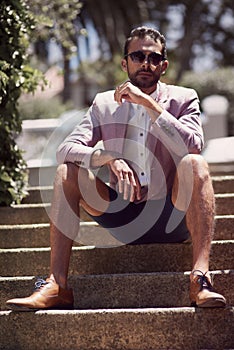 He makes it kinda hard not to stare. a well-dressed young man sitting outside on a staircase.