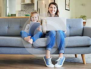 She makes working from home fun. a young mother and daughter using a laptop and digital tablet on the couch at home.