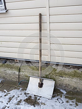 A makeshift metal wide snow shovel is propped against the wall