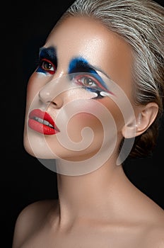 Makeup art theme: beautiful girl with blue and red make-up and white hair on a dark isolated background in studio