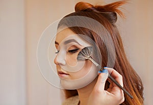 Makeup artist applied with a brush blush on the girl`s face, concludes the daily make-up in a beauty salon.