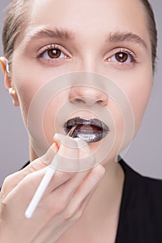 Makeup artist applies black lipstick. Hand of make-up master, painting lips of young beauty model girl .