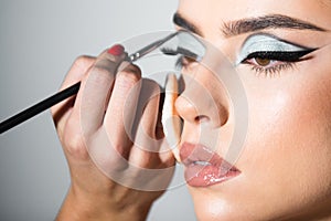Makeup artist applies eye shadow. Hand of visagiste, painting cosmetics of young beauty model girl. Cosmetology, beauty