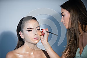 Makeup artist applies eye shadow. Hand of visagiste, painting cosmetics of young beauty model girl. Fashion shiny