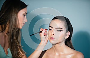 Makeup artist applies eye shadow. Hand of visagiste, painting cosmetics of young beauty model girl. Fashion shiny