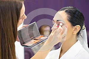 Makeup artist applies makeup to beautiful young girl holding set of cosmetics