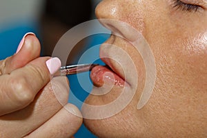 Makeup artist applies pink lipstick shine. Beautiful female face. Hand of a make-up master painting lips of a young girl beauty