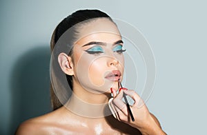 Makeup artist applies red lipstick. Hand of make up master, painting lips of young beauty model girl. Girl model with