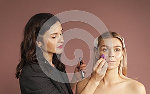 Makeup artist applies skintone with Sponge makeup egg on nude model woman face. Perfect makeup