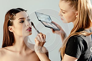 Makeup artist applying concealer on attractive model  on white