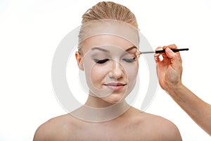 Makeup artist applying eye shadow for beautiful young woman on white background