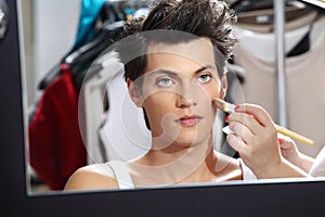 Makeup artist applying foundation with a brush, man in the dressing room mirror