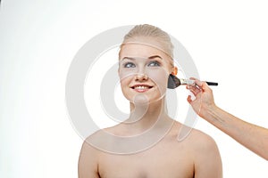 Makeup artist applying powder for beautiful young woman on white background