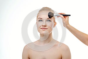 Makeup artist applying powder for beautiful young woman on white background