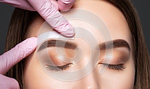 Makeup artist does facial hair removal procedure. Beautiful girl having Permanent Make-up on her Eyebrows. The make-up artist does