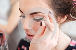 Makeup artist doing false lashes to young woman in curlers