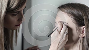 Makeup artist doing makeup for eyebrows. Young girl doing professional makeup, eyebrow shaping