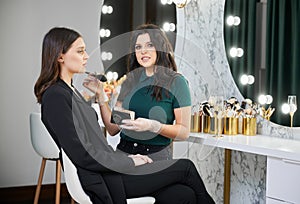 Makeup artist doing makeup for young woman in beauty salon.
