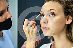 Makeup artist doing professional make up of young woman creating look in beauty salon close up. Vogue, cosmetics and glamour