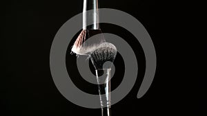 Makeup artist hit brush to create blow of powder over black background