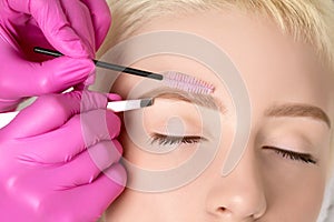 Makeup artist plucking eyebrows with tweezers to a beautiful woman with short blonde hair and with healthy clean skin. Women`s