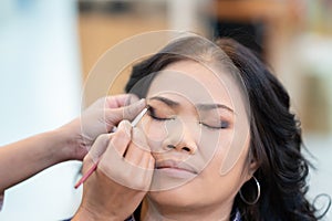 Makeup artist preparing Middle age asian woman face undergoing eyebrow correction procedure, Closeup shot eye makeup with brush