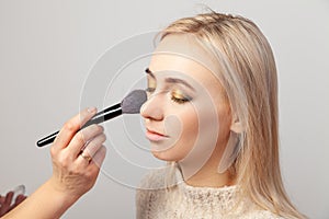 Makeup artist puts make-up on a blonde model with eyes closed, overlay the shadows in the Oriental styleholds a brush in her hands