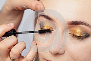 Makeup artist puts on an oriental-style make-up with gold and green shades of a young attractive blonde girl, paints her eyelashes