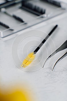 Makeup artist's tools for eyelash extension tweezers, brush for combing yellow color lie on light background. MOCKUP