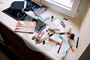 Makeup artist set. Eyeshadow palette, makeup brushes, mascara and eyelash curler on the windowsill by the window.