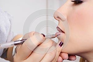 Makeup artist tracing red contour on the lips