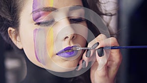 Makeup artist uses brush to apply lipstick to model`s lips. Model with false lashes and face art painting preparing to