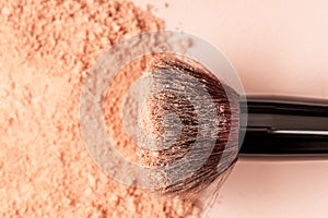 Makeup brush and loose beige powder against a background of sun glare. Powder texture, cosmetic peach background with