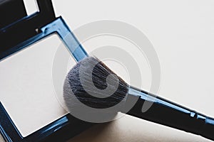 Makeup brush picking up compact face powder close-up. Decorative cosmetics on a beige background. Makeup artist workflow