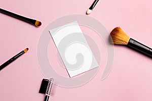 Makeup brush and white business card on pink background. A horizontal template for a makeup artist's business card