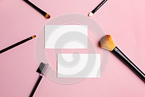 Makeup brush and white business card on pink background. A horizontal template for a makeup artist's business card