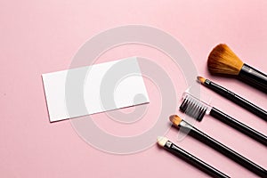 Makeup brush and white business card on pink background. A horizontal template for a makeup artist's business card