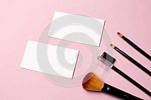 Makeup brush and white business card on pink background. A horizontal template for a makeup artist's business card