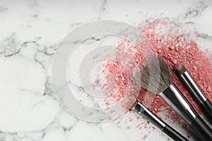 Makeup brushes and scattered blush on white marble table, flat lay. Space for text