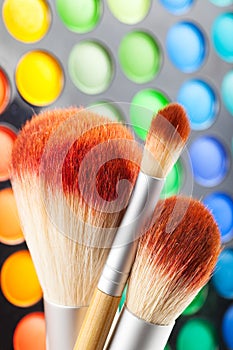 Makeup brushes and set of colorful eye shadows as background